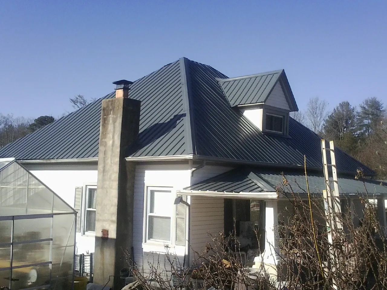 Dark blue standing seam metal roof on a white farmhouse with dormer — Slate & Tile Roof Repair by Roofing Brothers in Potterville