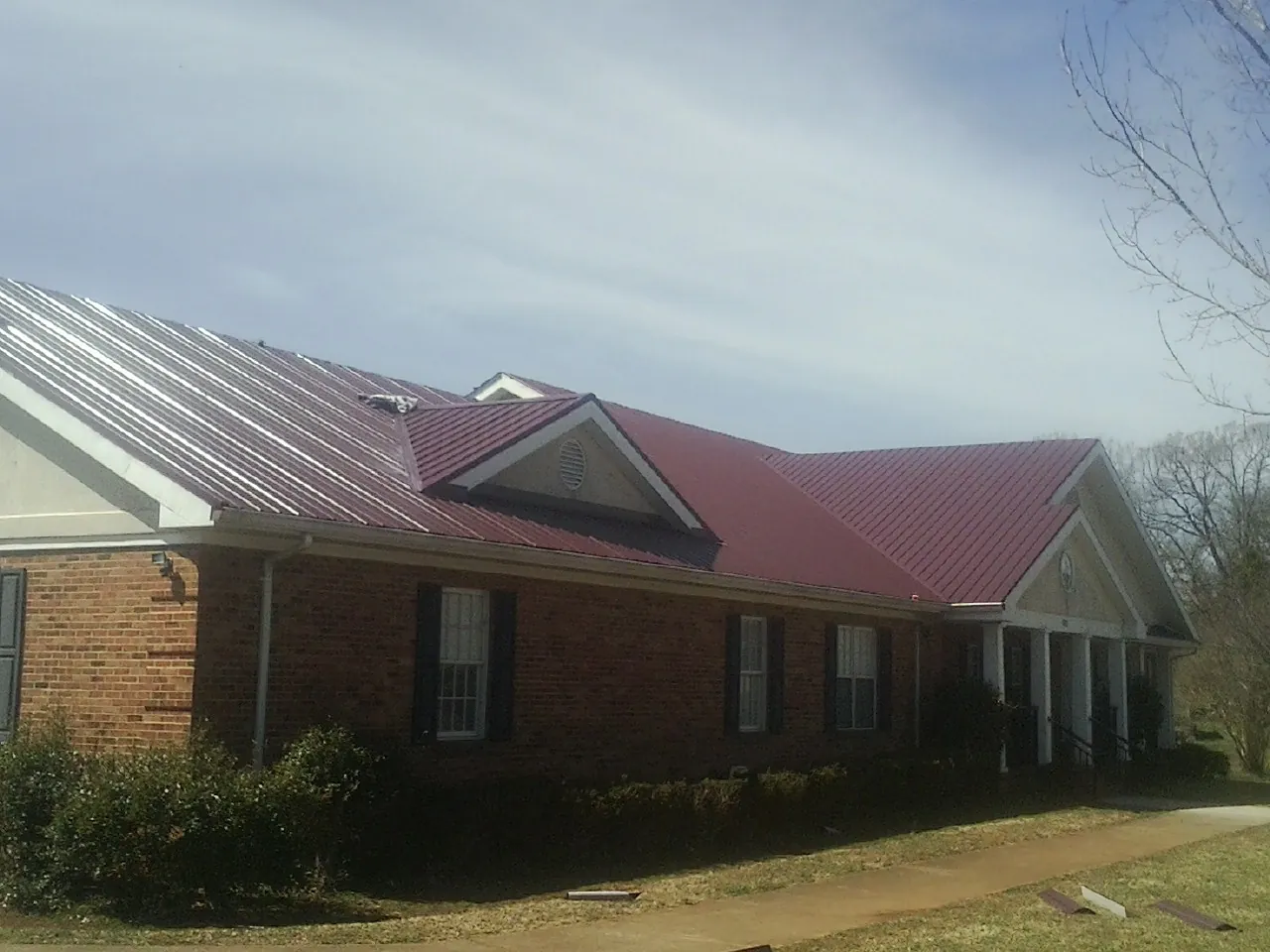 Red metal roof with gabled entries on a long brick building, from a Hail Damage Roof Repair job in Potterville