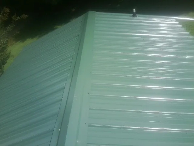 New green metal panels meeting at the ridge of a roof — Flat Roof Repair work by our crew in Potterville