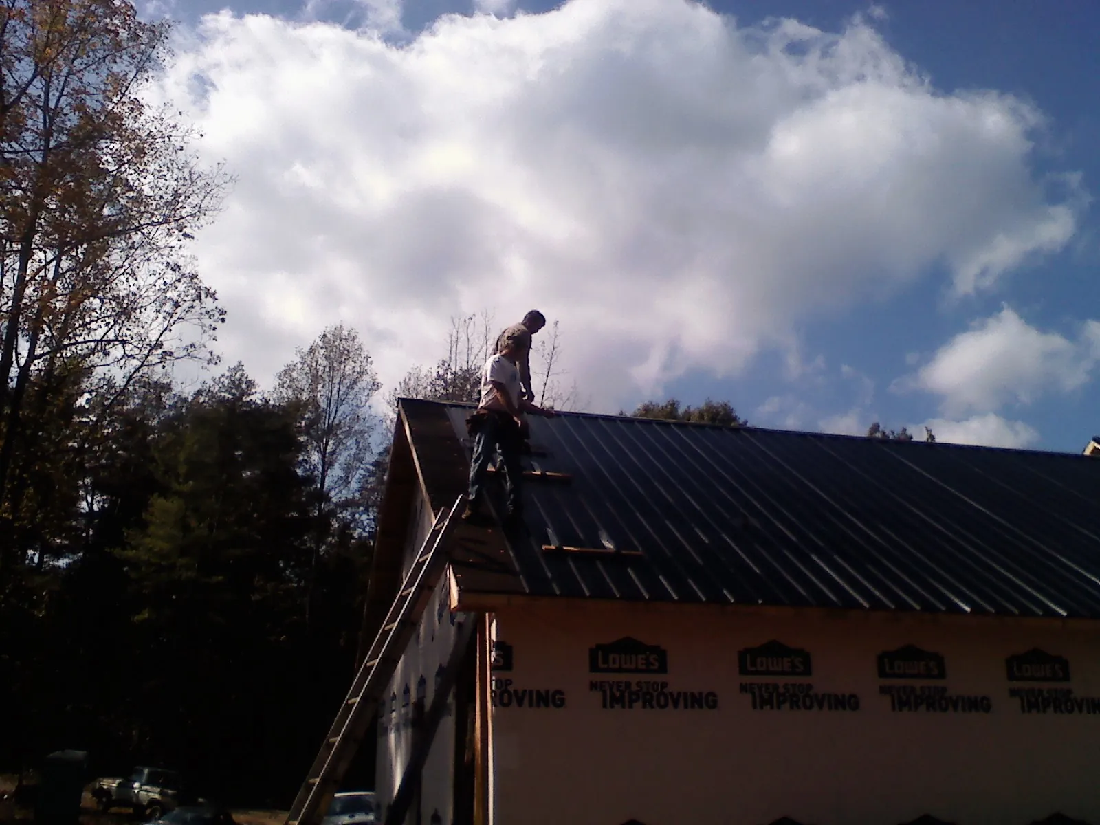 Roofer fastening dark metal panels high against a cloudy sky, from a Roof Inspection job in Potterville