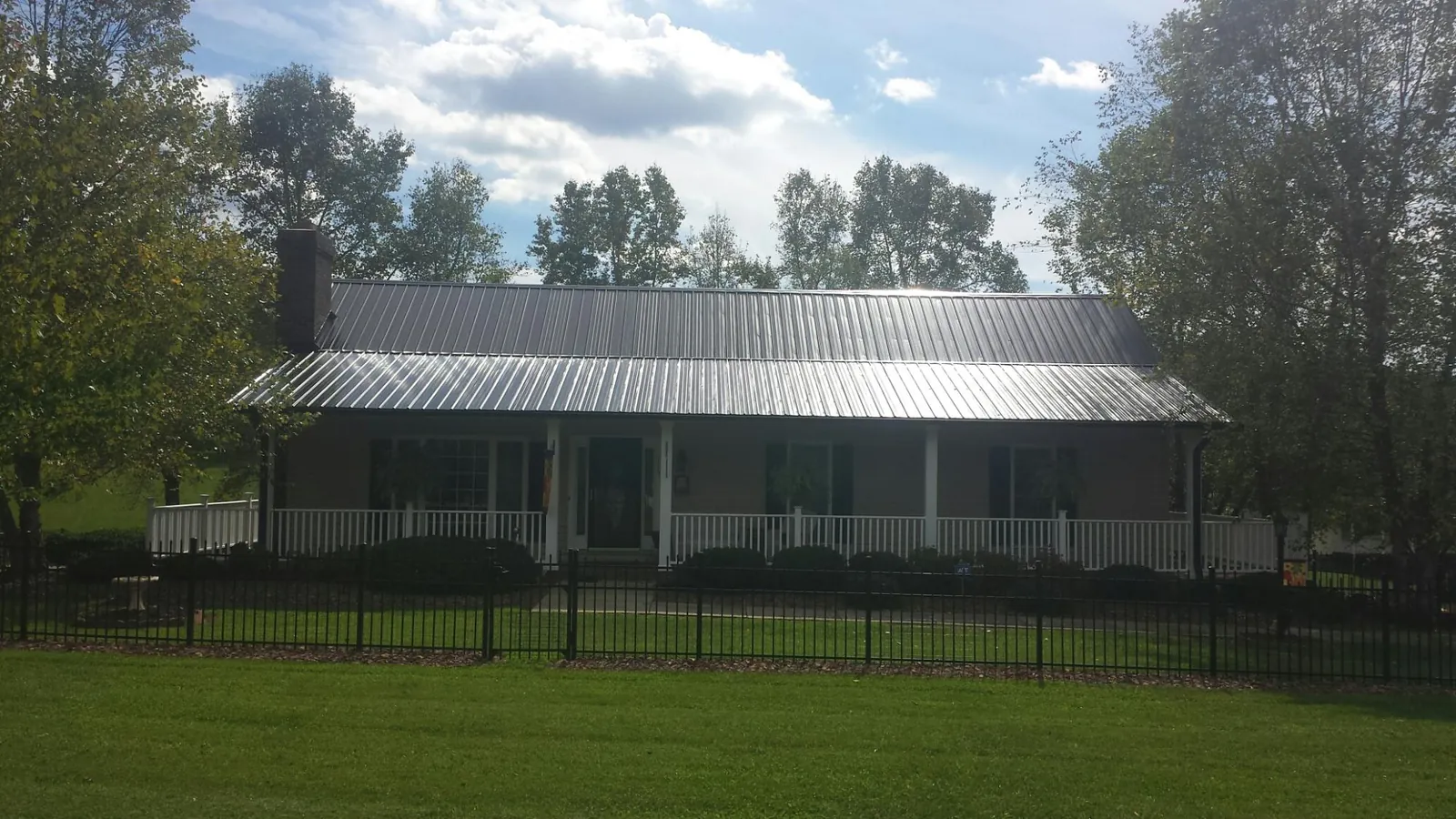 Gray metal roof on a brick ranch with a full width front porch — Gutter Guard Installation work by our crew in Potterville