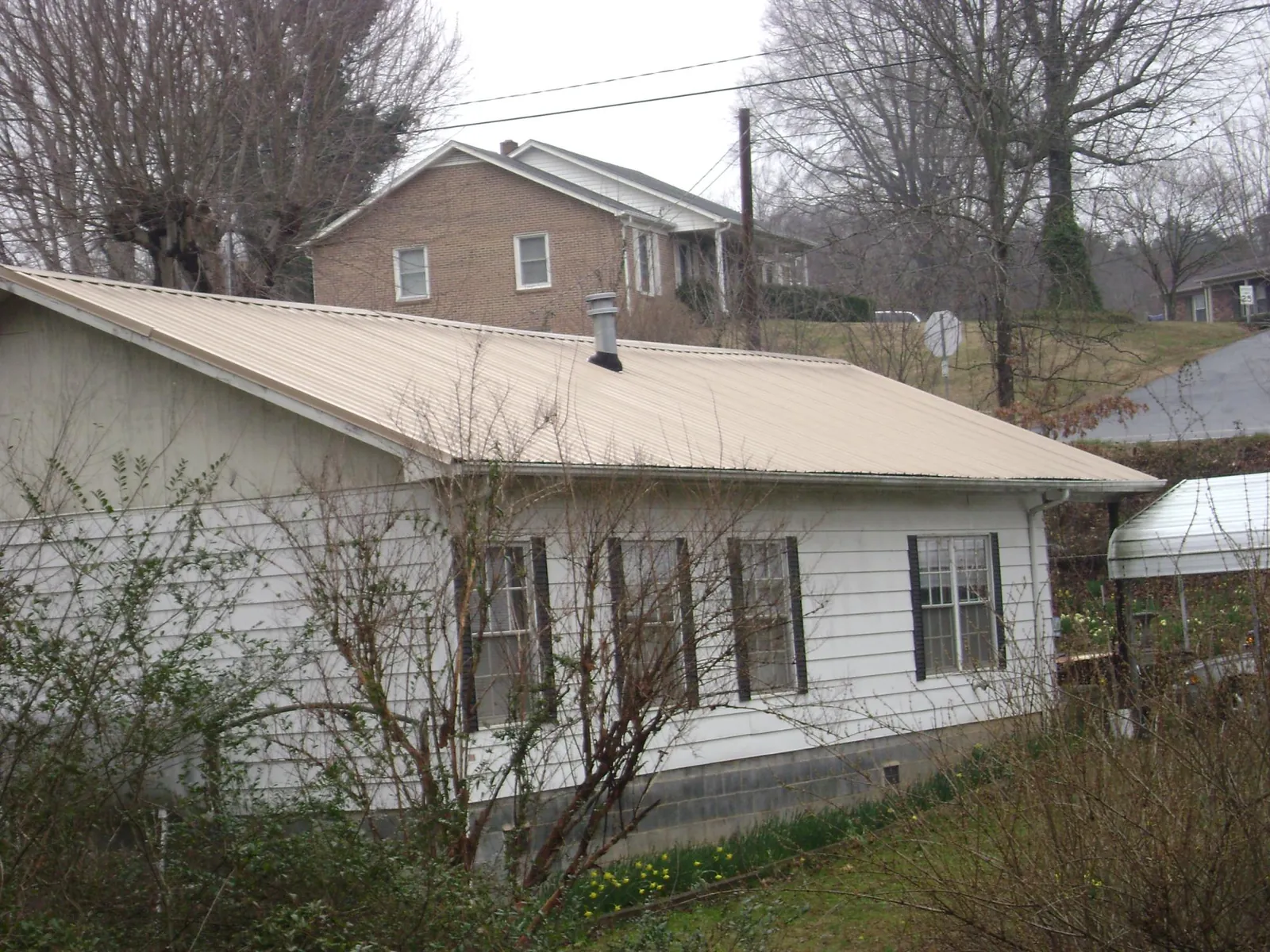 Tan metal roof on a white sided house set into a hillside — Commercial Roofing by Roofing Brothers in Potterville