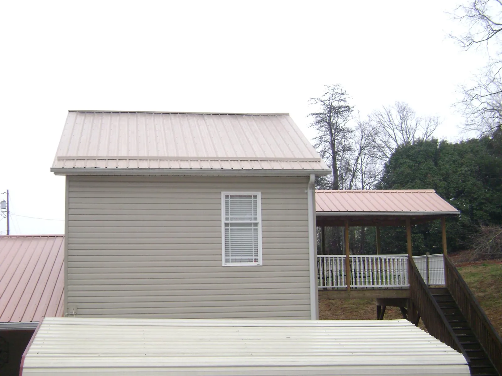 Tan metal roofs on a two story addition and attached porch, from a Roof Replacement job in Potterville